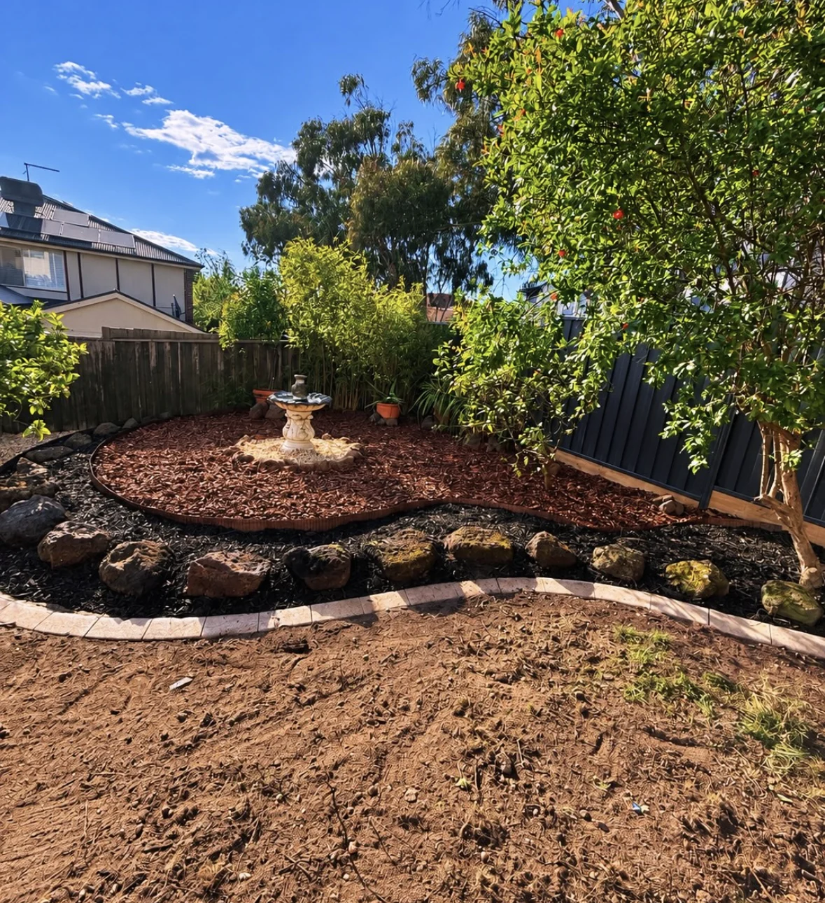 Curved garden bed with rock edging, established trees and fresh mulch