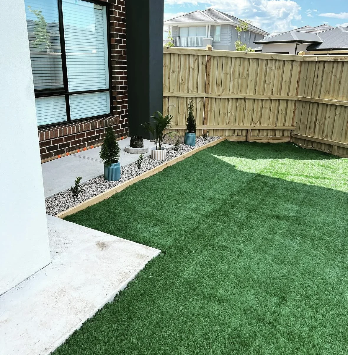 Artificial lawn bordered by a concrete path and neat planting beside a brick home